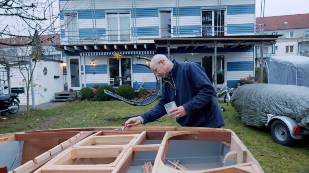 
			Heiner lakuje na zahradě díly své dřevěné lodě

		